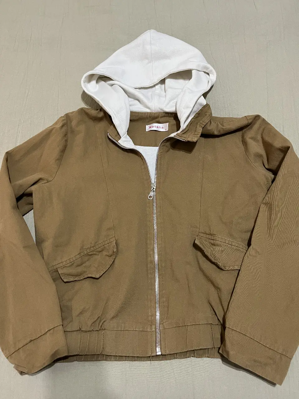 Campera marrón con capucha blanca. Tiene cierre frontal y bolsillos delanteros. Ideal para un look casual y cómodo.
