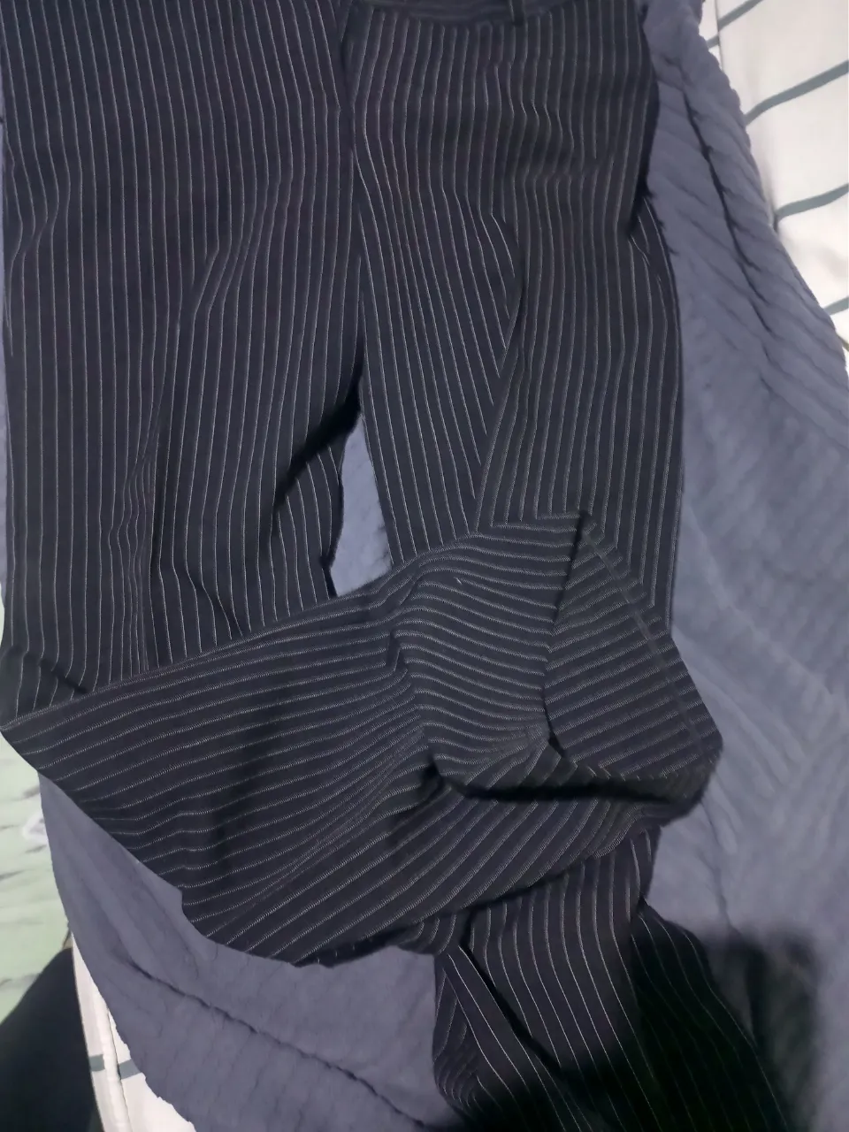 Pantalón de vestir a rayas verticales finas blancas sobre fondo negro. Presenta un dobladillo en la parte inferior de una de las piernas.