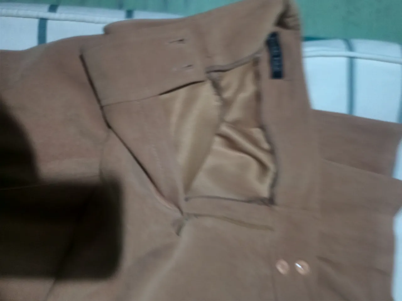 Pantalón de color marrón claro, con cierre y botón en la cintura. Posee bolsillos frontales.