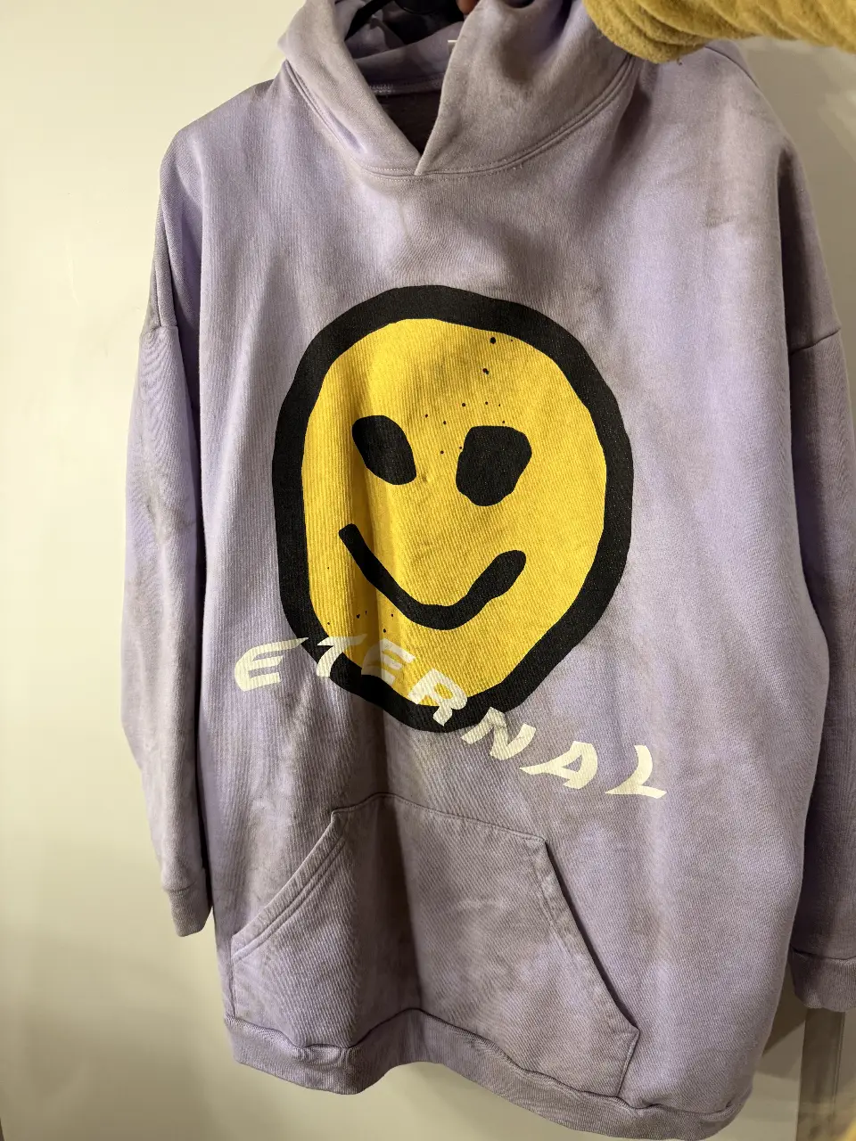 Buzo canguro oversize frizado de color lila con estampado de carita sonriente en amarillo y negro. Estilo streetwear, ideal para un look casual y cómodo.