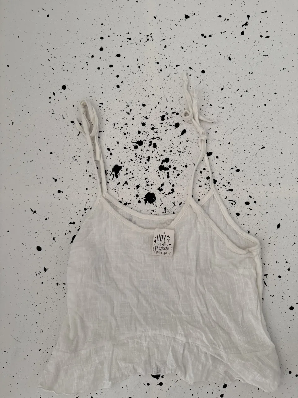 Musculosa blanca con tiras finas y volado en el ruedo. Tiene un pequeño detalle de etiqueta con estampa.