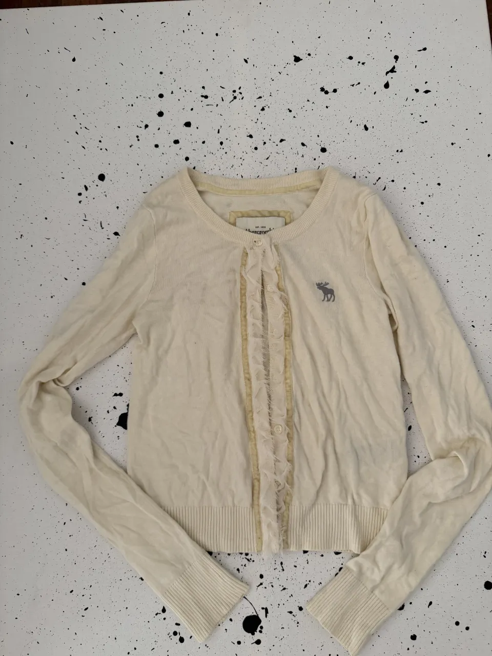 Cardigan color crema con volados en el frente y botones.