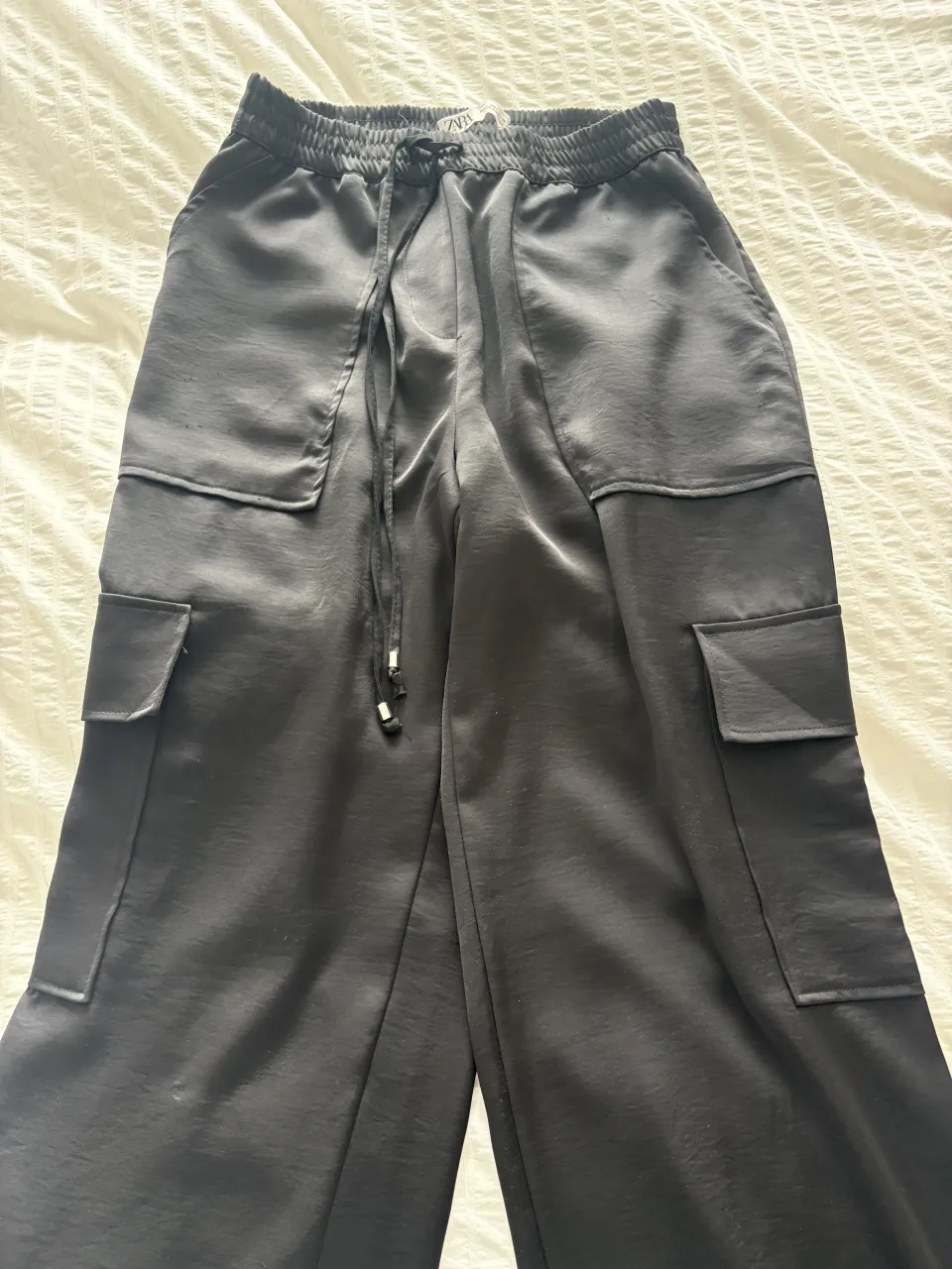 Pantalón cargo de seda negro con cintura elastizada y cordón de ajuste. Posee bolsillos cargo en los laterales y en la parte trasera.