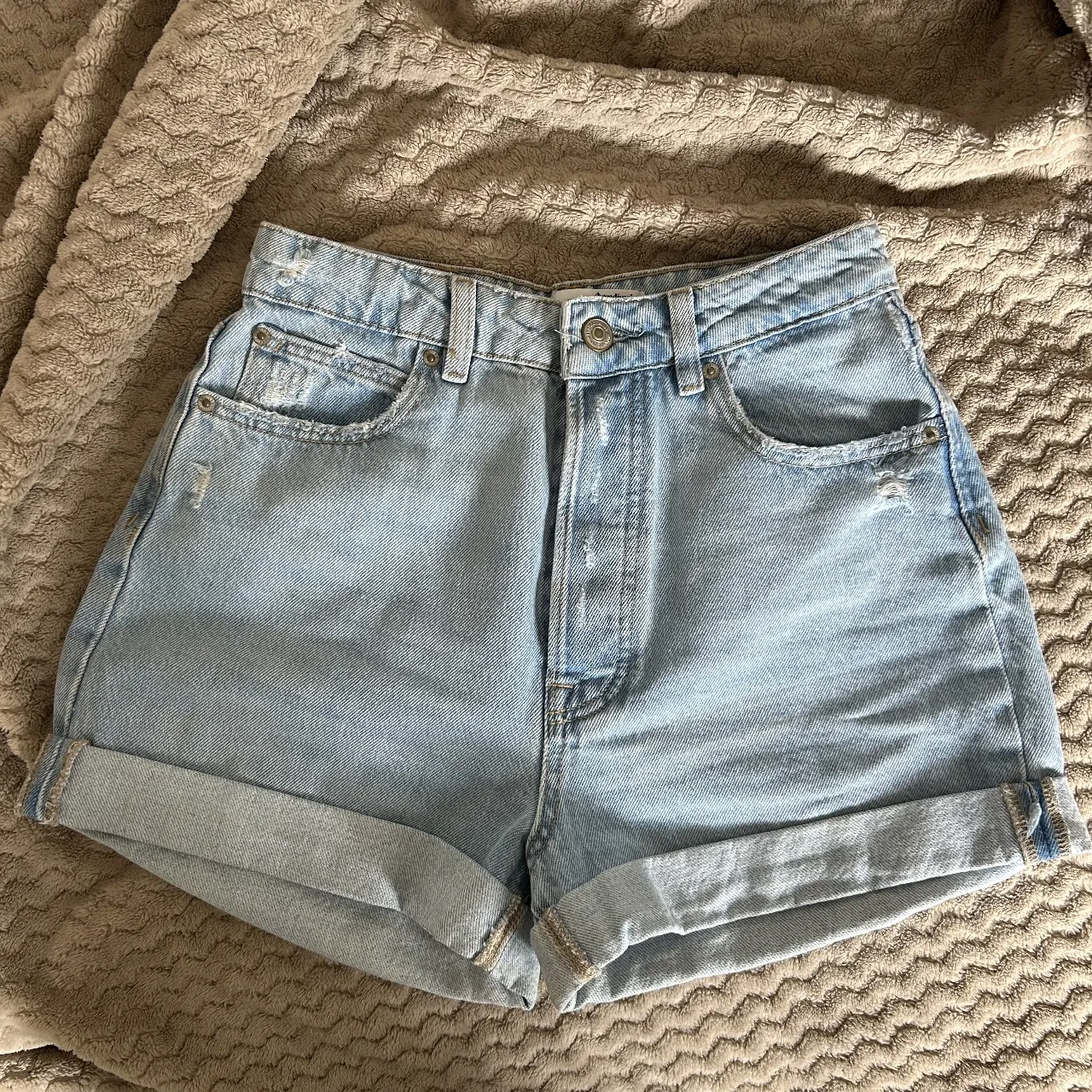 Shorts de jean tiro alto, color celeste claro, con roturas y detalles desgastados. Poseen dobladillo en los bajos y son ideales para un look casual de verano.