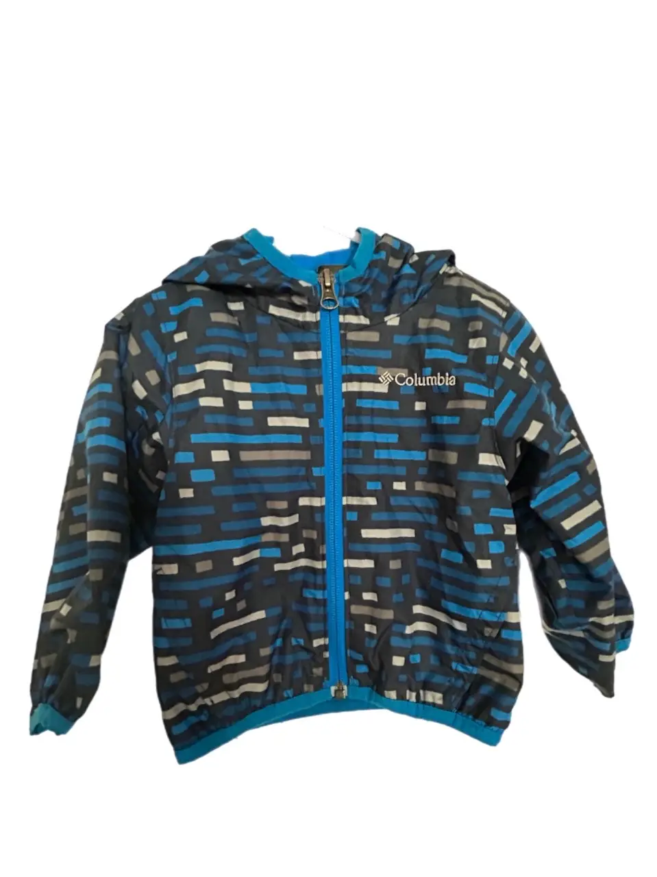 Campera Columbia para niño, con estampado geométrico en tonos azules y grises. Con capucha, cierre frontal y forro interior azul. Ideal para proteger del viento y la lluvia ligera.