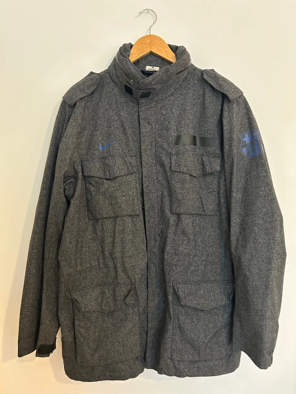 Campera deportiva gris con logo de Nike y escudo del Barcelona en la manga. Talle L. Ideal para uso casual o deportivo.