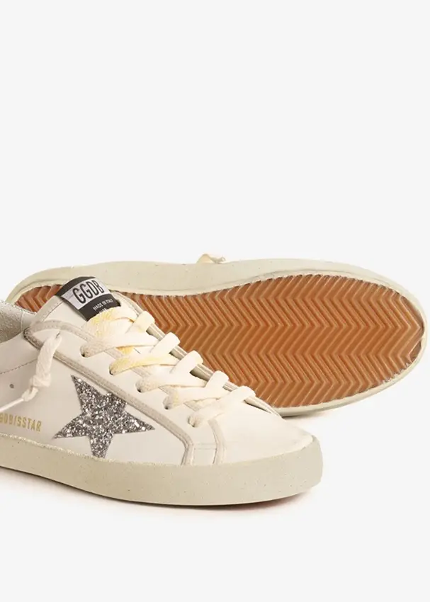 Zapatillas Golden Goose Super-Star Classic con estrella de glitter plateada. Talle 35. Blancas con detalles desgastados, cordones amarillentos y suela marrón. Incluye caja, bolsa de tela y papel.