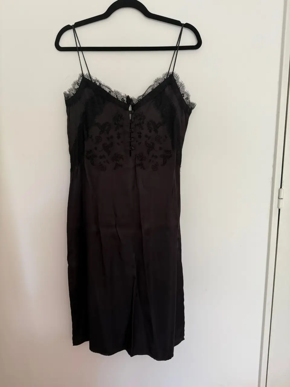 Vestido mini negro de satén con detalles de encaje en el escote y tirantes finos. Ideal para una salida nocturna o evento especial.