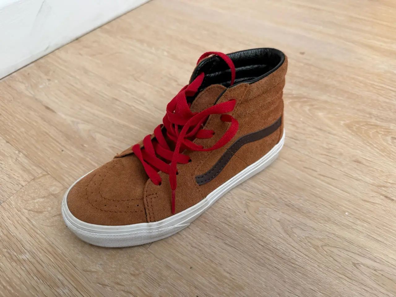 Zapatillas Vans Sk8-Hi de gamuza marrón con cordones rojos y suela blanca. Un clásico de la moda urbana, ideales para un look casual y con estilo.