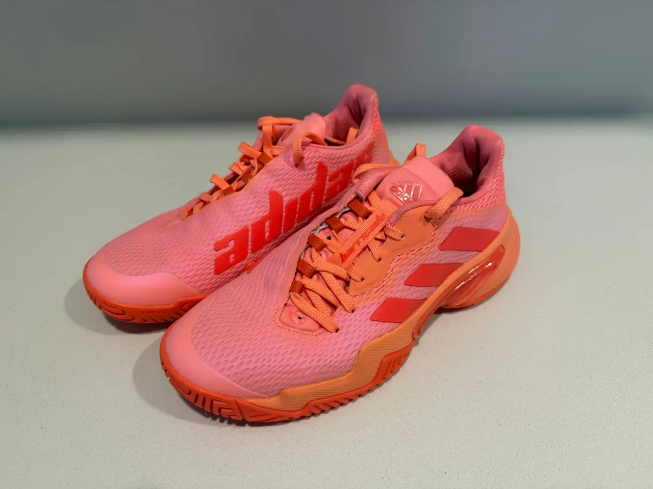 Zapatillas de tenis Adidas color rosa y naranja, ideales para la práctica deportiva. Con un diseño moderno y cómodo, estas zapatillas ofrecen un excelente agarre y soporte para tus partidos.