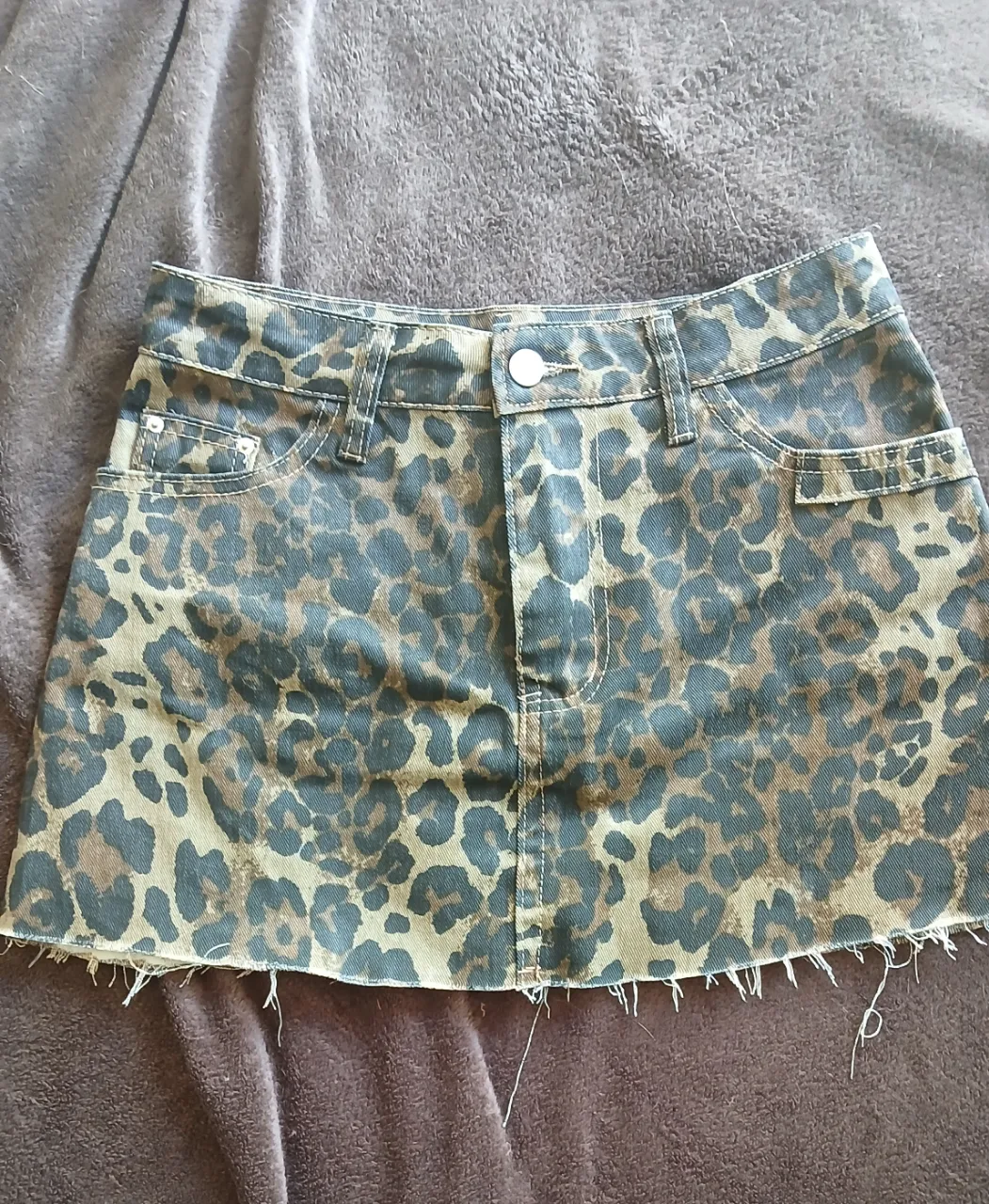 Pollera de jean corta con estampa animal print de leopardo. Tiene detalles desgastados en el borde inferior y bolsillos.