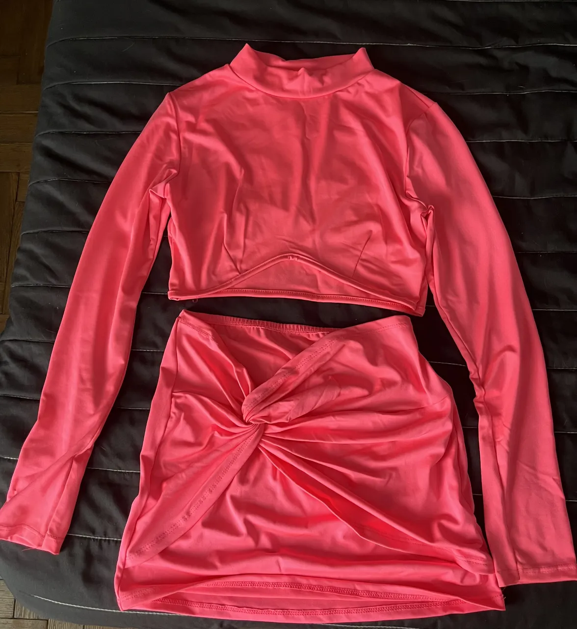 Conjunto de dos piezas color rosa flúor. Incluye un top manga larga con cuello alto y una falda corta con nudo delantero.