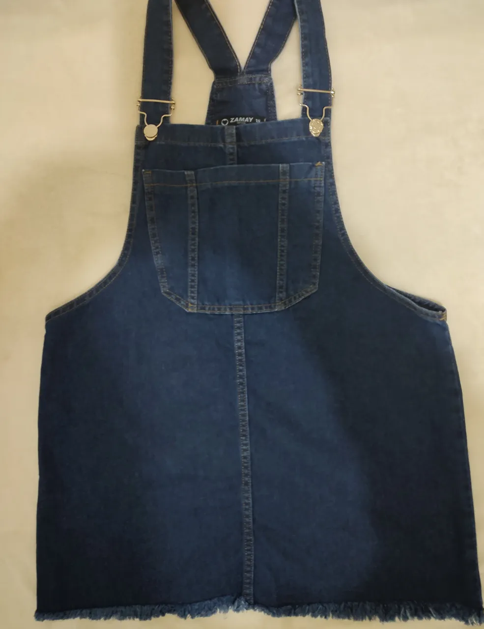 Vestido jardinero de jean azul, con flecos en el borde inferior. Posee tirantes ajustables y un bolsillo en el pecho. Ideal para un look casual y moderno.