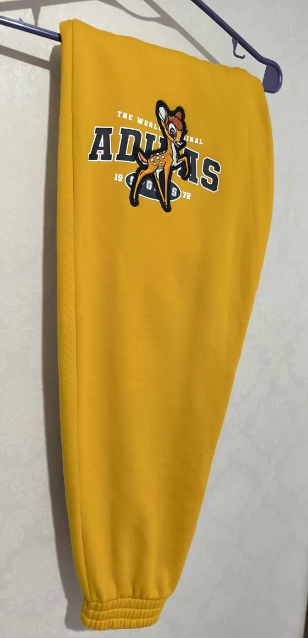 Pantalón de jogging mostaza con estampa de Bambi y logo de Adidas.