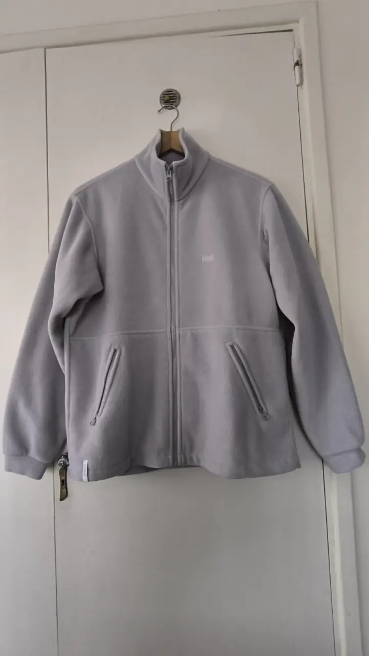 Buzo Níquel de polar gris, ideal para el invierno. Posee dos bolsillos delanteros y el logo de la marca bordado en el pecho. Perfecto para un look casual y abrigado.