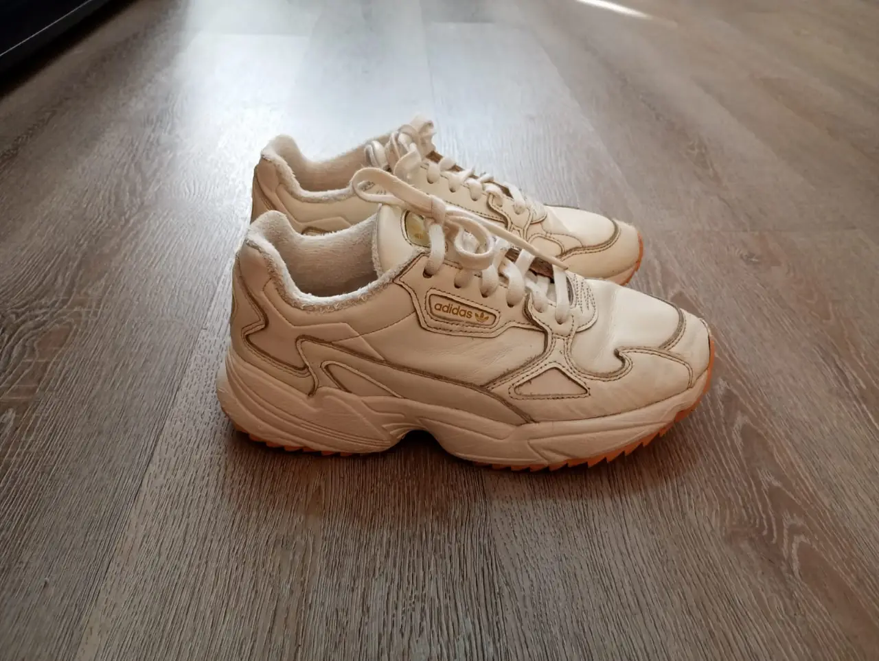 Zapatillas Adidas Falcon blancas, con detalles en dorado y suela rosa. Ideales para un look casual y cómodo.