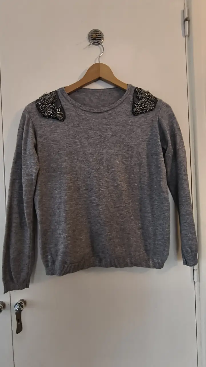 Sweater gris de mujer con detalles plateados en los hombros. Ideal para un look elegante y sofisticado.