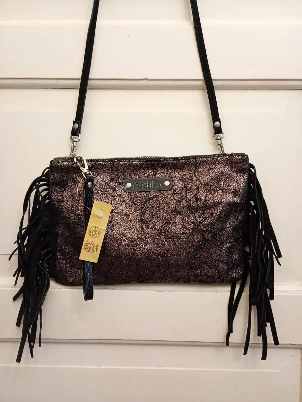 Cartera bandolera de cuero con flecos, color marrón con detalles metalizados. Marca Astica.