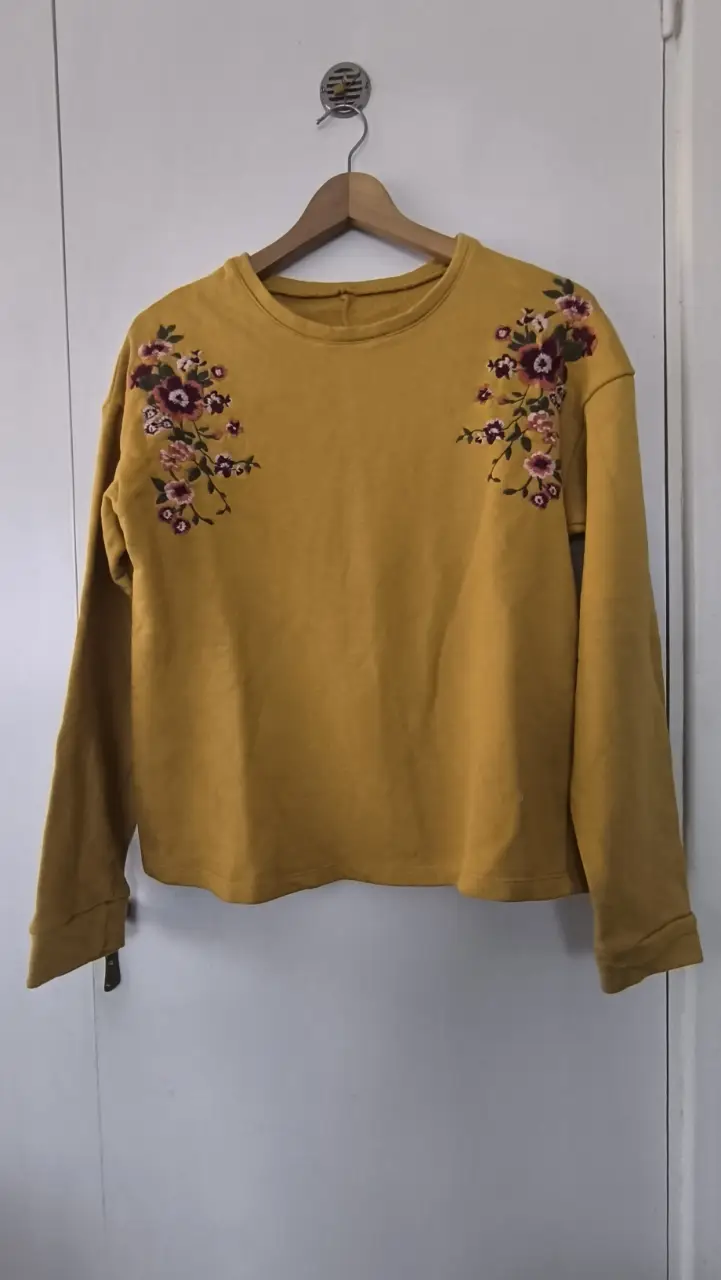 Buzo de cuello redondo color mostaza con bordado floral en los hombros. Ideal para un look casual y cómodo.