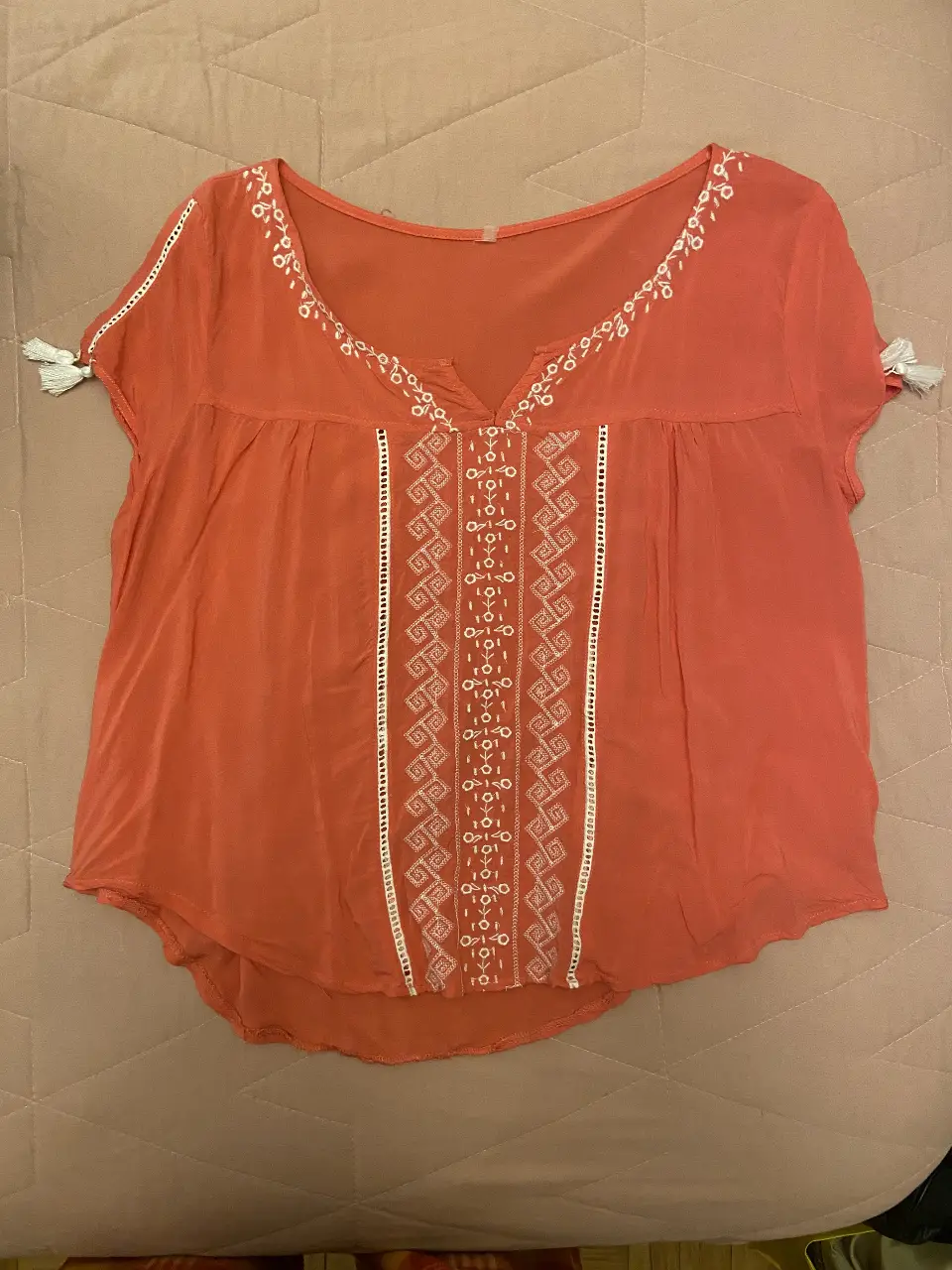 Blusa de color coral con detalles bordados en blanco. Diseño con cuello en V y mangas cortas con borlas. Ideal para un look casual y fresco.