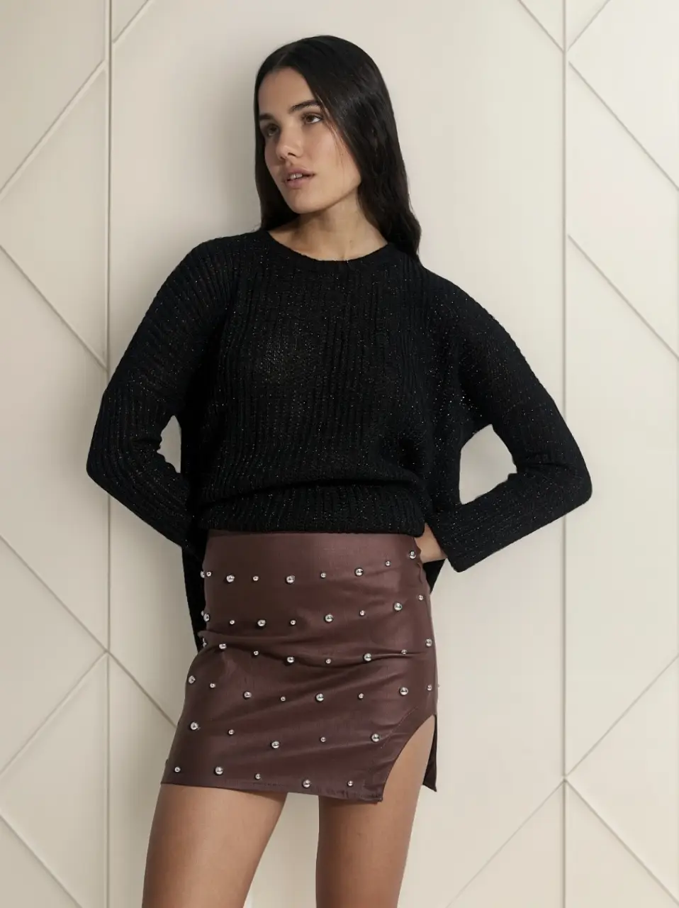 Minifalda de cuero sintético marrón con detalles de tachas plateadas. Diseño de abertura trasera con cierre. 