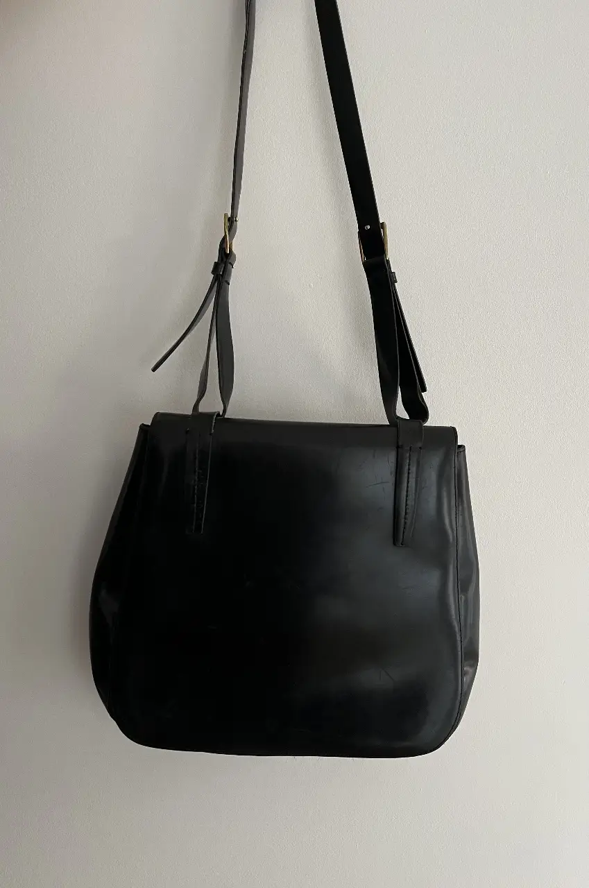 Cartera bandolera negra de cuero, con solapa y correa ajustable. Ideal para uso diario.