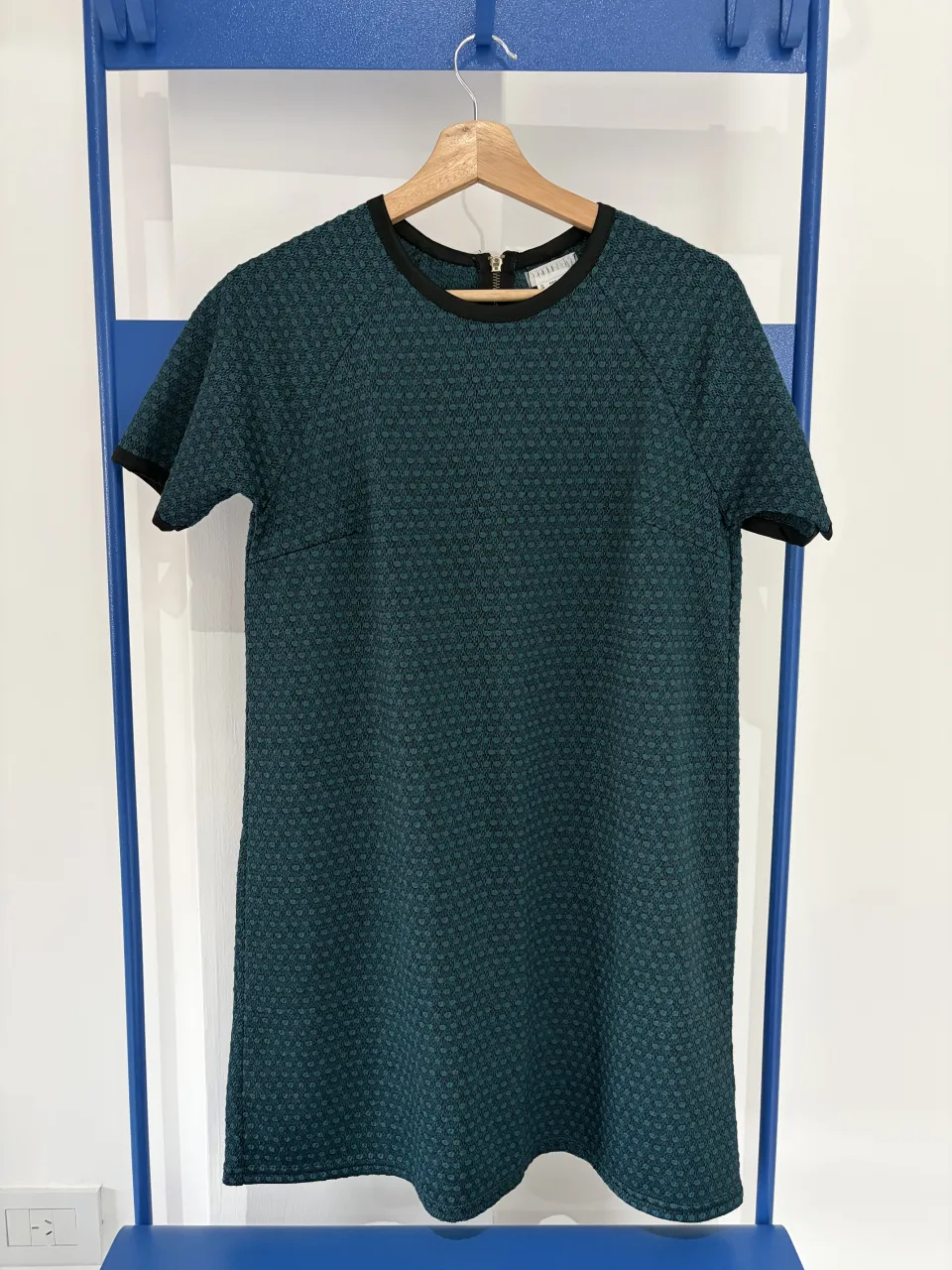 Vestido importado corto de tela texturizada con estampa geométrica en tonos verde oscuro y negro. Posee cuello redondo con detalle negro y cierre metálico en la espalda. Ideal para un look casual y moderno.