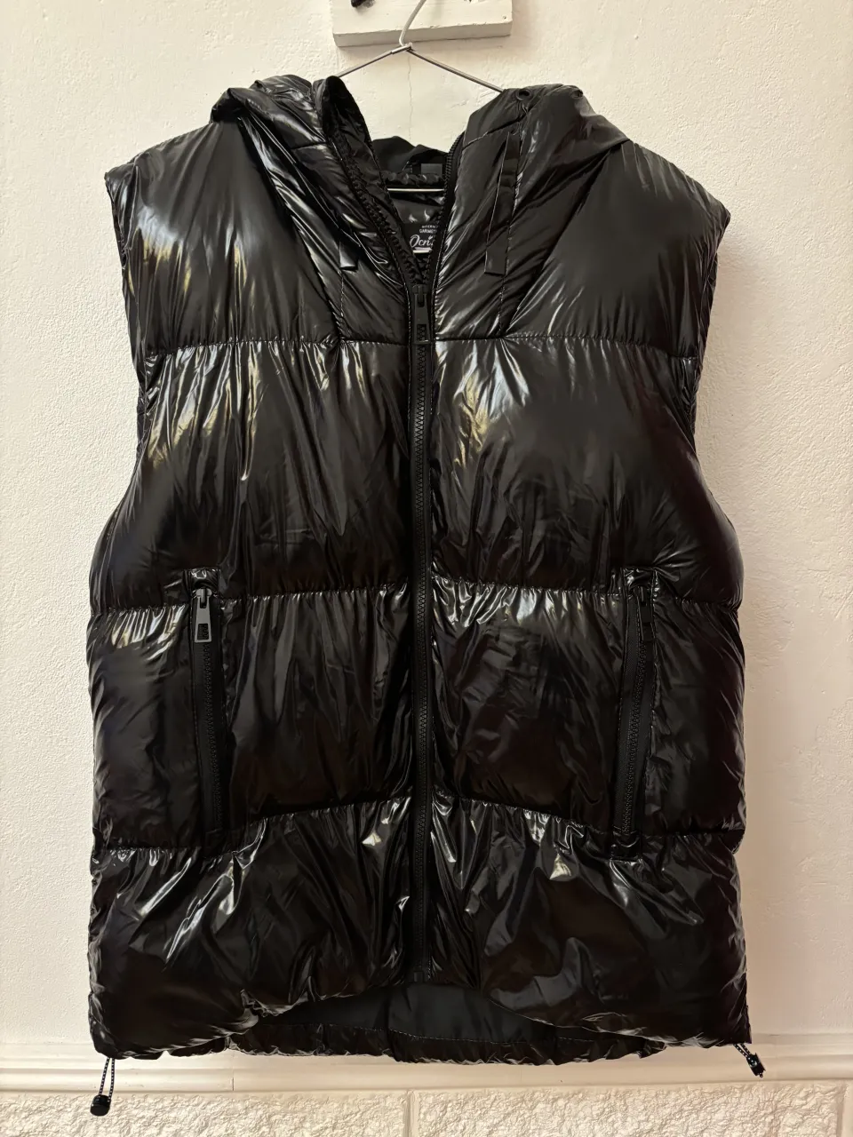 Chaleco puffer negro brillante con capucha. Ideal para un look urbano y moderno, perfecto para los días frescos de entretiempo o como capa adicional en invierno. Su diseño acolchado y el acabado brillante le dan un toque canchero y a la moda.