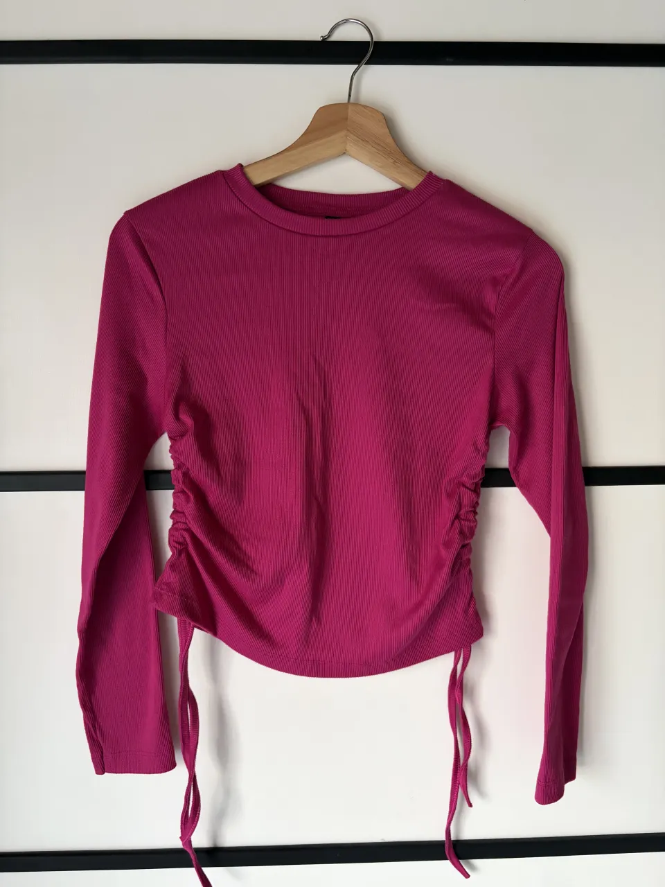 Remera manga larga de color fucsia con fruncido y cordones ajustables a los costados. Posee cuello redondo.