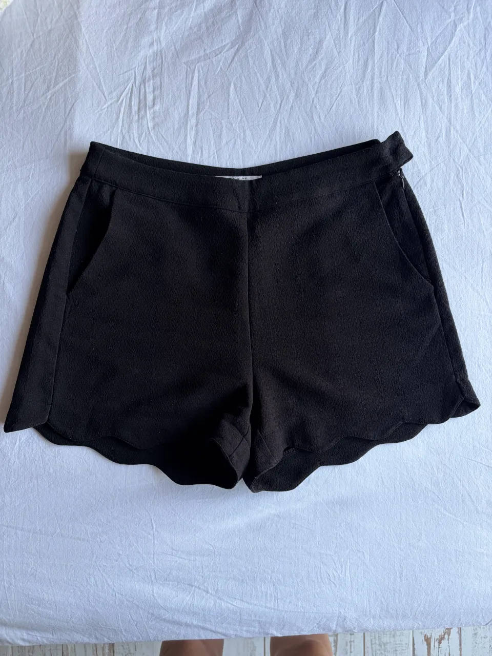 Shorts negros con terminación de ondas. Tiro alto, con bolsillos laterales y detalle de hebilla en la cintura.