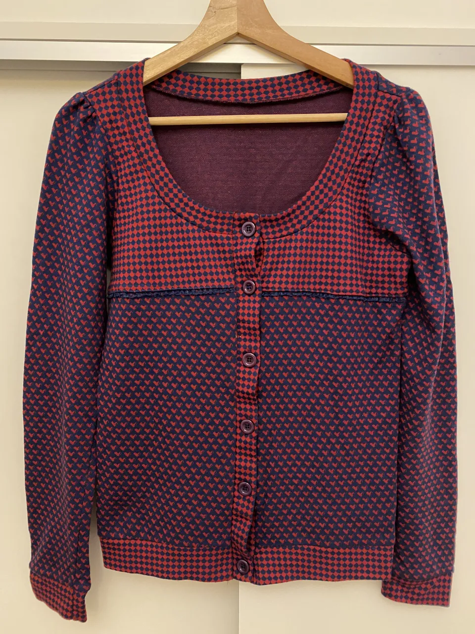 Cardigan de tejido liviano con estampa de rombos y corazones en tonos azul marino y rojo. Posee botones al frente y cuello redondo. Ideal para un look casual y cómodo.