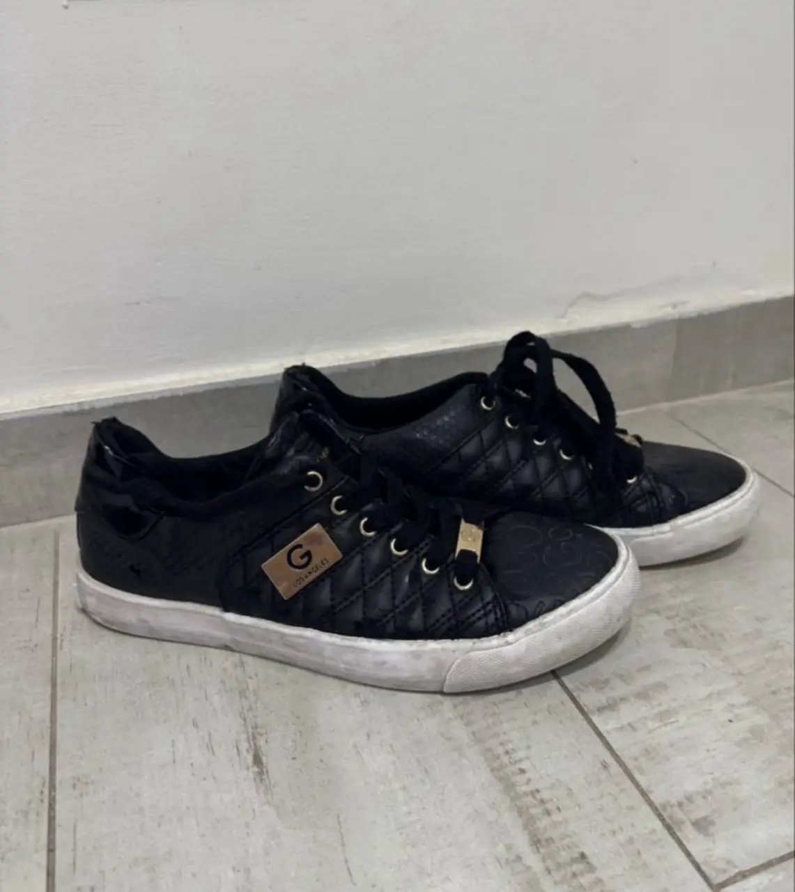Zapatillas Guess negras con detalles dorados y suela blanca. Diseño acolchado y logo de la marca.