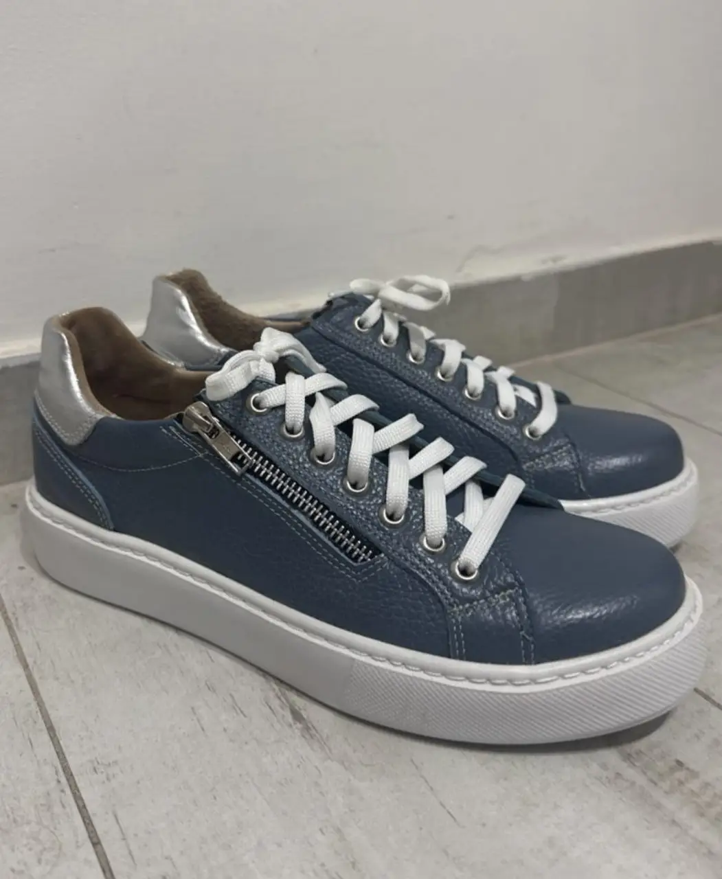 Zapatillas de mujer azules con detalles plateados y cierre lateral. Suela blanca. Ideales para un look casual y cómodo.