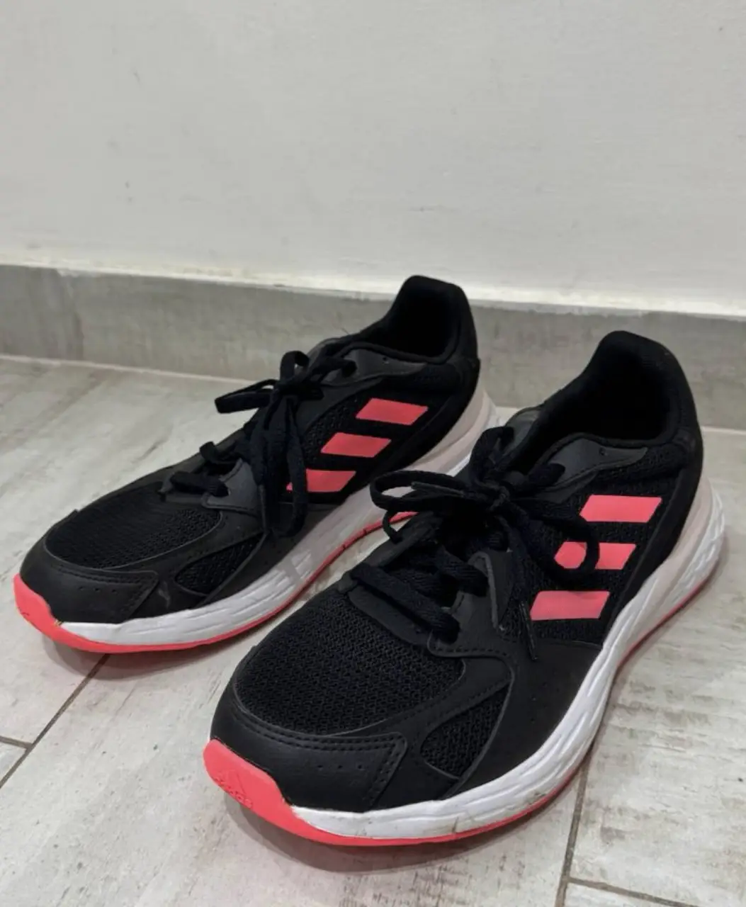 Zapatillas Adidas negras con detalles en rosa. Ideales para running y actividades deportivas. Tienen suela blanca y detalles de la marca.