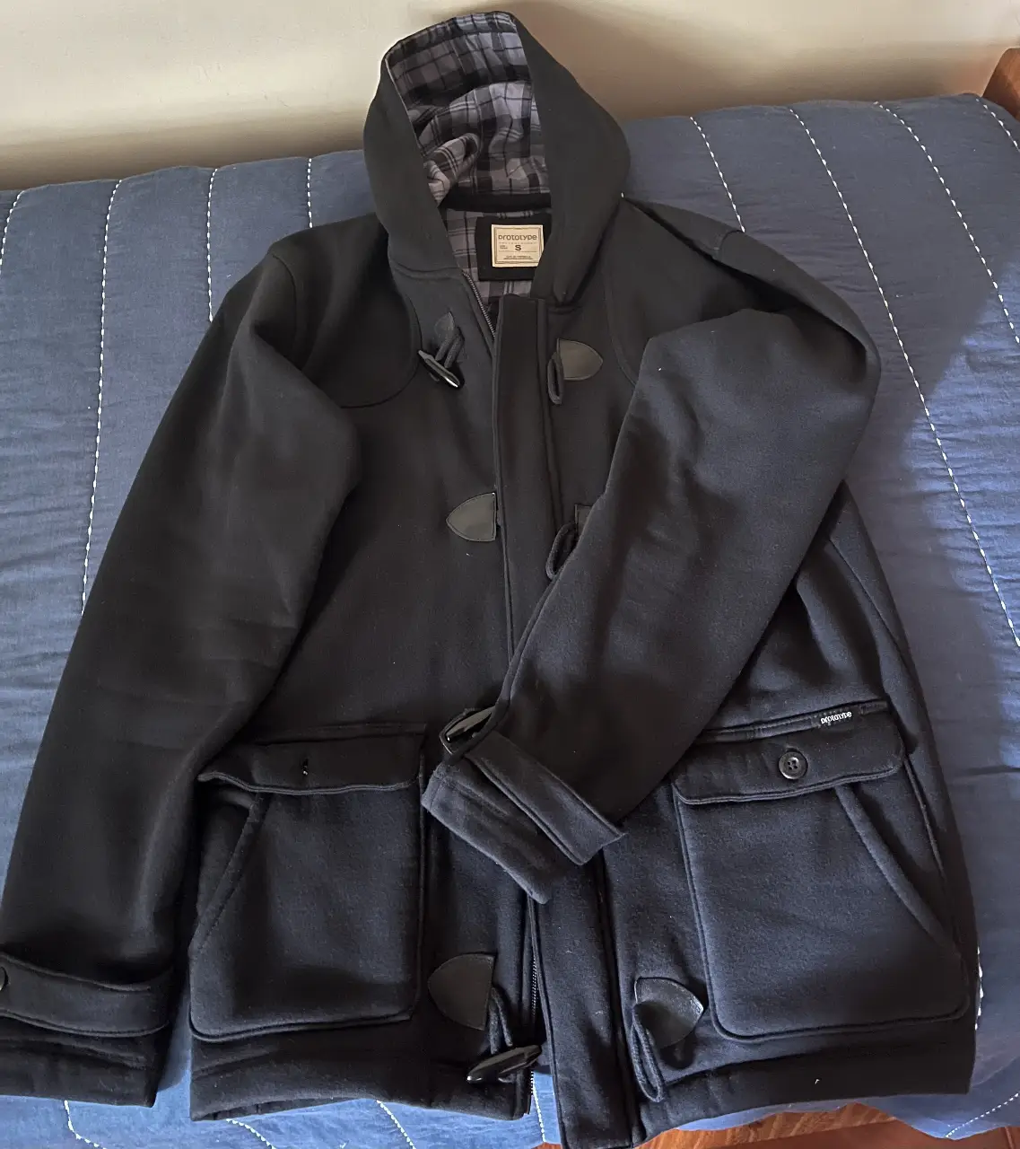 Campera negra de hombre, estilo duffle coat, con capucha y detalles de botones de madera. Ideal para el invierno.