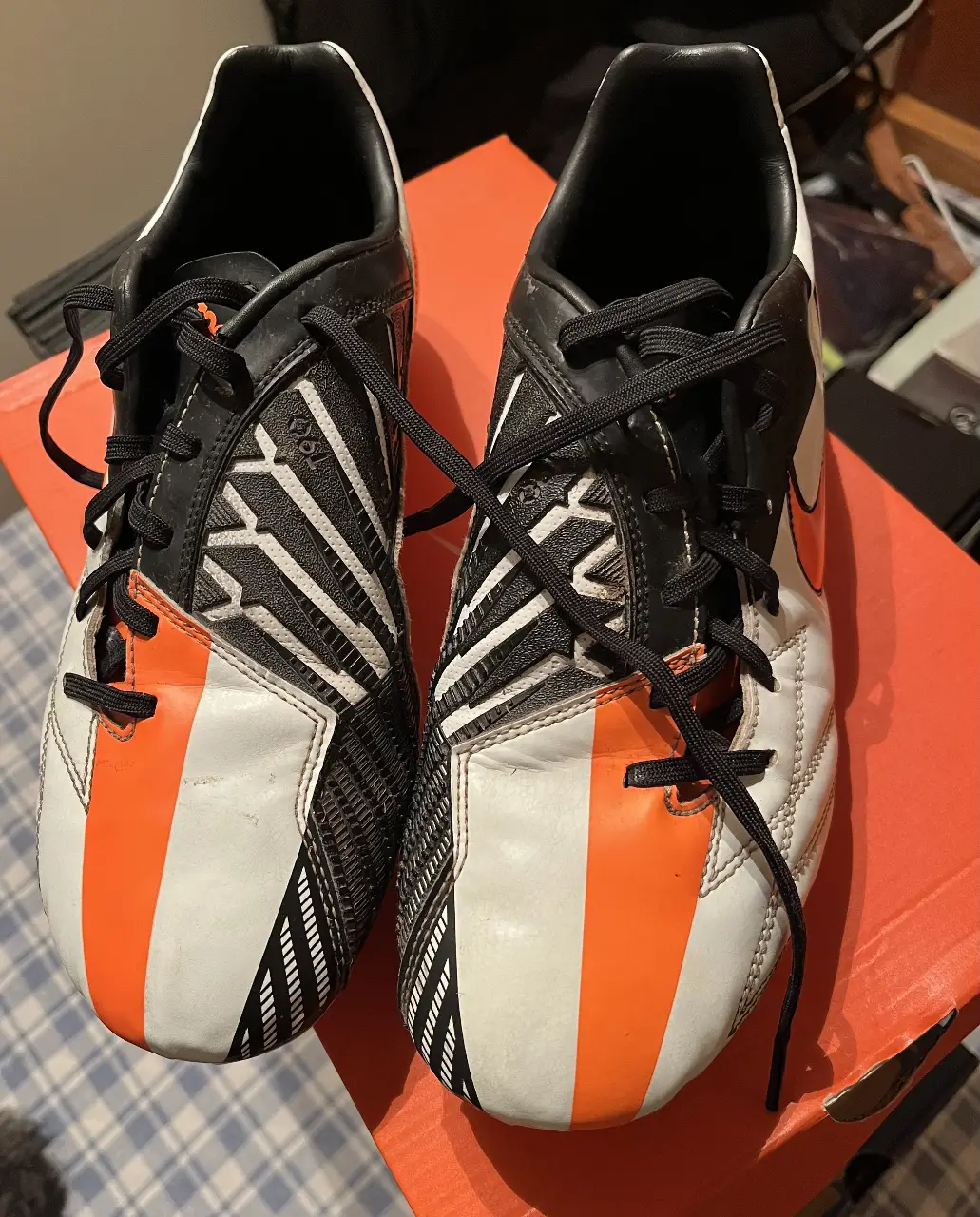Botines de fútbol Nike T90, blancos con detalles en negro y naranja. Ideales para jugar en césped.