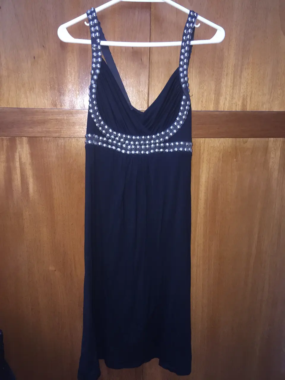 Vestido negro corto con detalles brillantes en el escote y tirantes. Ideal para fiestas y eventos especiales. Diseño elegante y sofisticado.
