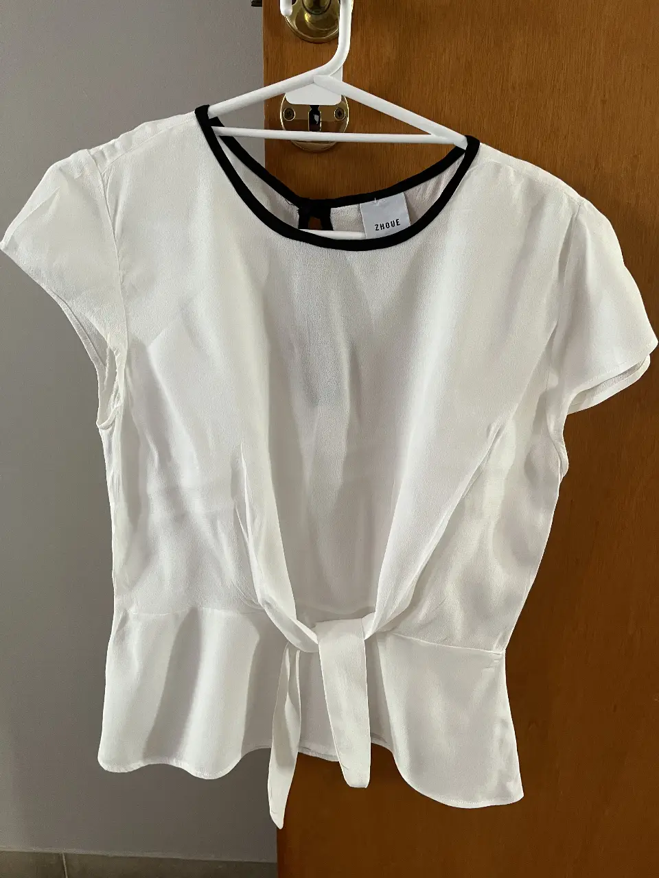 Blusa blanca con detalle de lazo en la cintura y cuello negro. Ideal para un look elegante y versátil.
