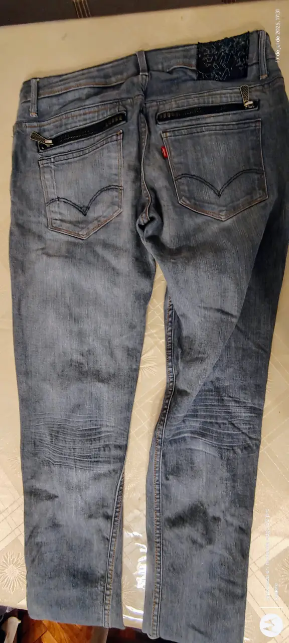 Jeans  recto, de color azul claro, con detalles de cierres en los bolsillos traseros y en los tobillos. Un clásico para cualquier ocasión.