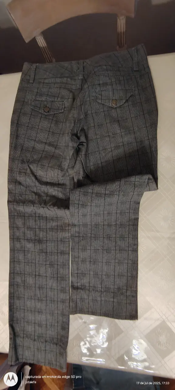 Pantalón sastrero de mujer, color gris con diseño a cuadros. Posee dos bolsillos traseros con botones y cierre con botón y cremallera. Ideal para un look formal o de trabajo.