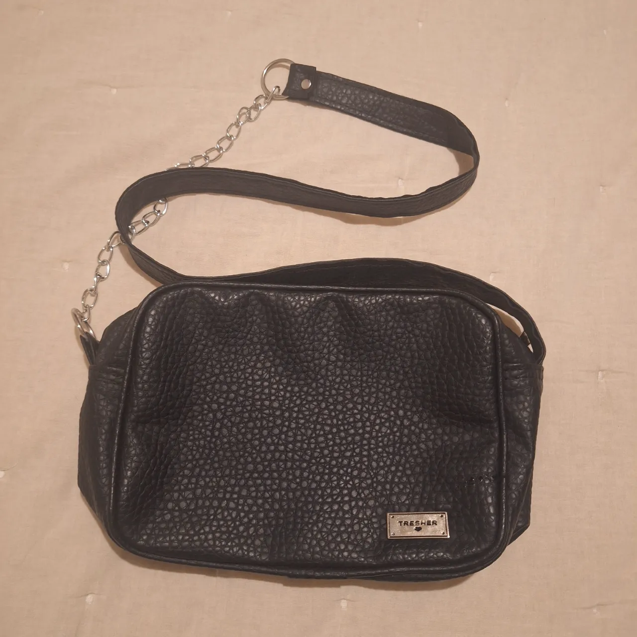 Bandolera negra de cuero sintético con correa ajustable y cadena decorativa. Cuenta con un compartimento principal y un bolsillo interno. Ideal para llevar lo esencial con estilo.