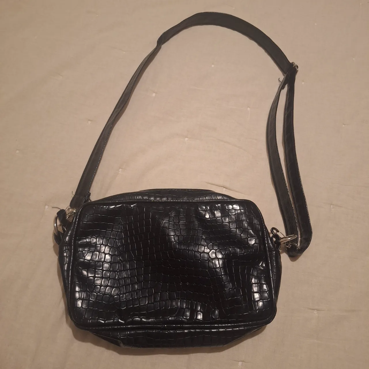 Bandolera negra con diseño de reptil, ideal para llevar tus esenciales con estilo. Cuenta con correa ajustable y cierre para mayor seguridad. Perfecta para un look moderno y versátil.