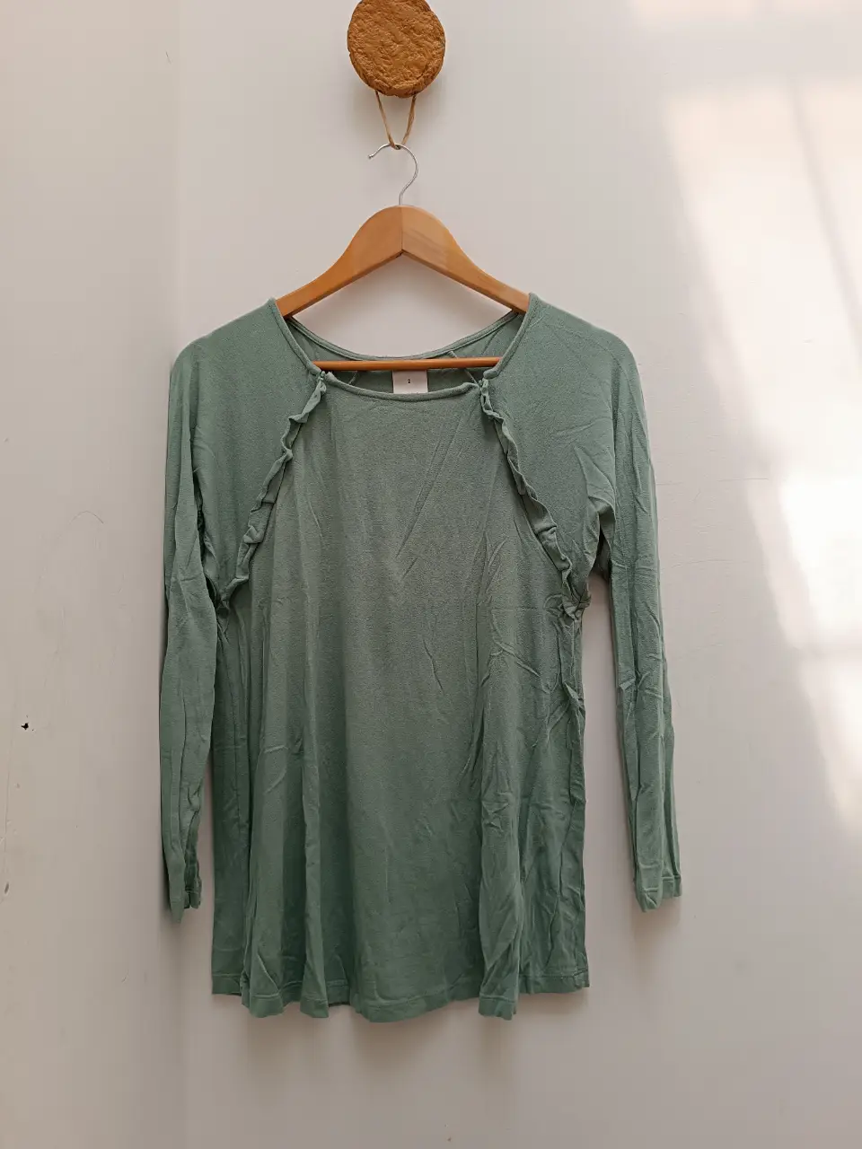 Remera manga larga verde agua con detalles de volados en el cuello y cierre lateral. Ideal para un look casual y cómodo.