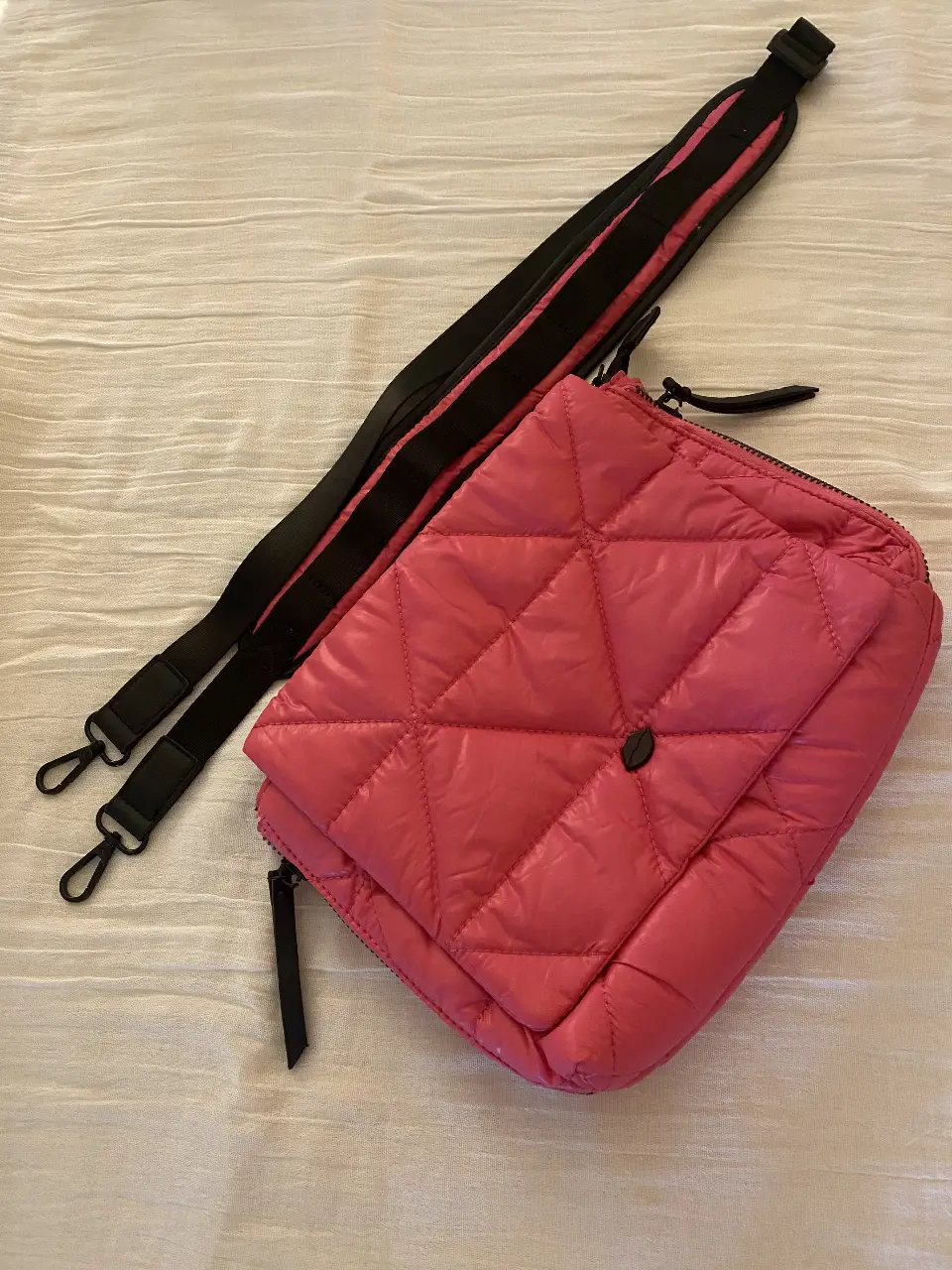 Cartera bandolera acolchada en color rosa. Cuenta con correa ajustable y cierre. Ideal para un look casual y moderno.