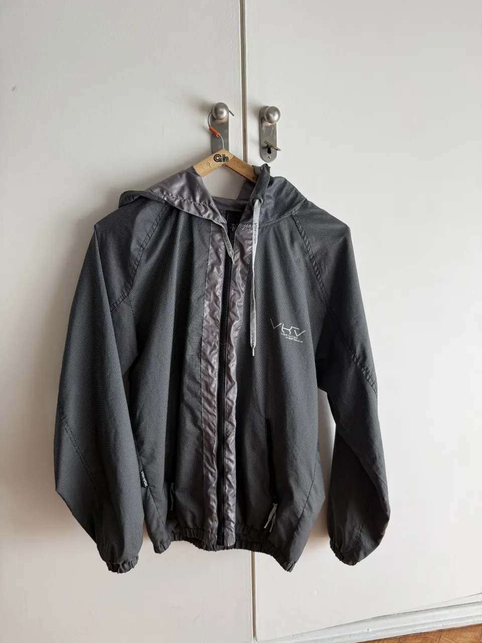 Rompevientos con capucha y cierre central. Posee detalles de tela satinada en el frente y en la capucha. Logo blanco bordado en el frente.