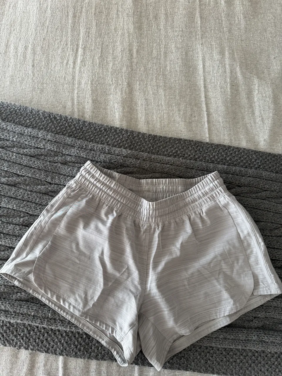 Shorts deportivos grises con finas rayas verticales en tono más claro. Cintura elastizada con cordón interno.