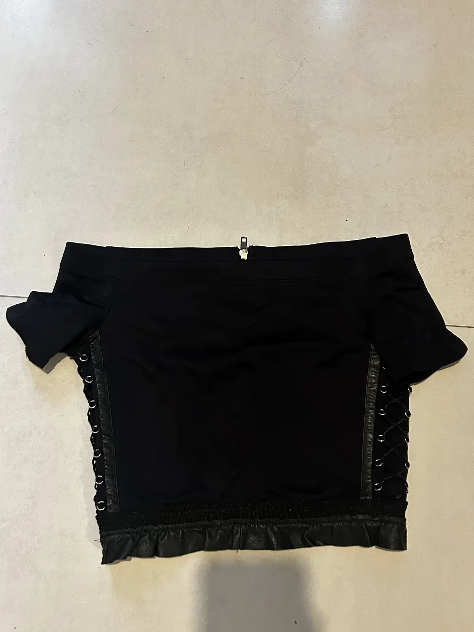 Top negro con diseño off shoulder, detalles de cuero y cierre en la espalda. Ideal para un look moderno y audaz.