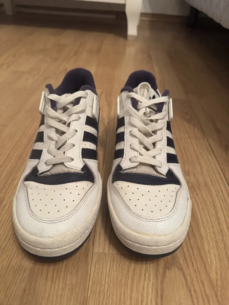 Zapatillas Adidas Forum Low blancas con detalles en azul marino. Diseño clásico y atemporal, ideales para un look casual y urbano.
