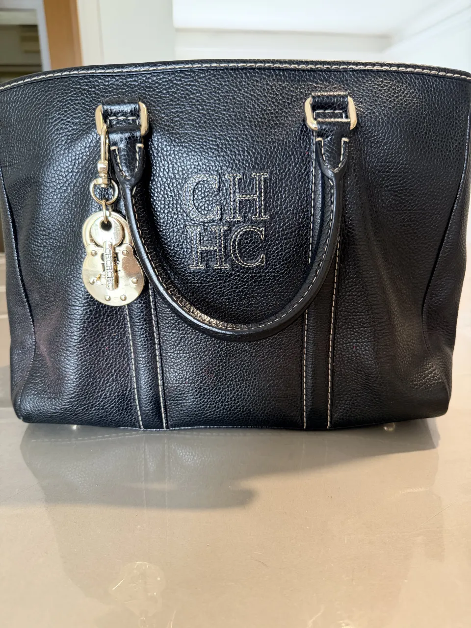 Bolso negro de cuero con logo CH bordado en el frente. Interior forrado en rojo vibrante con bolsillo interno con cierre. Ideal para el día a día o para complementar un look elegante.