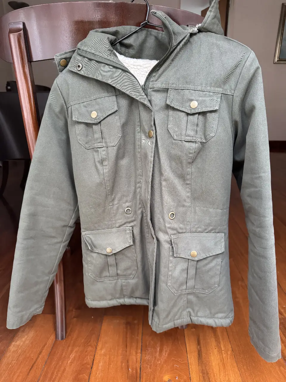Campera verde militar con capucha y forro de piel sintética. Posee múltiples bolsillos y cierre frontal. Ideal para el invierno.